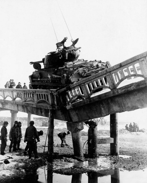 Men of the 8th Eng Bn, 1st Cav Div put logs under weakened support of a bridge near Yangzi, Korea, to prevent its collapse until a tank retriever can arrive and remove the M-4 tank. 28 Jan 1951